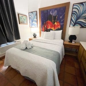 Standard Queen room at At Wind Chimes Boutique Hotel in San Juan, Puerto Rico — queen bed with vivid night-sky original artwork headwall, sage green coverlet, and terracotta tile floors