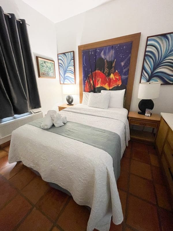 Standard Queen room at At Wind Chimes Boutique Hotel in San Juan, Puerto Rico — queen bed with vivid night-sky original artwork headwall, sage green coverlet, and terracotta tile floors