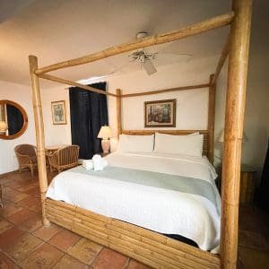 Accessible Deluxe King room at At Wind Chimes Boutique Hotel in San Juan, Puerto Rico — bamboo four-poster bed, terracotta tile floors, and rattan furnishings with Caribbean boutique charm