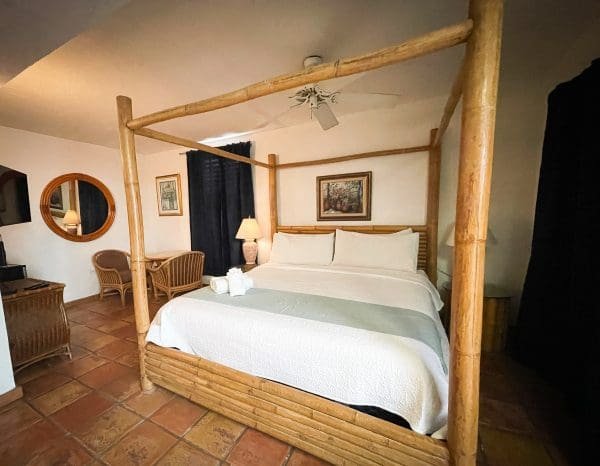 Accessible Deluxe King room at At Wind Chimes Boutique Hotel in San Juan, Puerto Rico — bamboo four-poster bed, terracotta tile floors, and rattan furnishings with Caribbean boutique charm